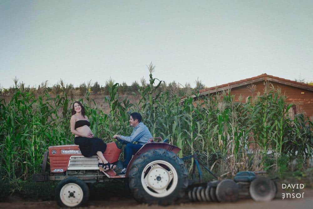 Expecting parents laughing together on a tractor in a cornfield — relaxed, candid family session by David Josué