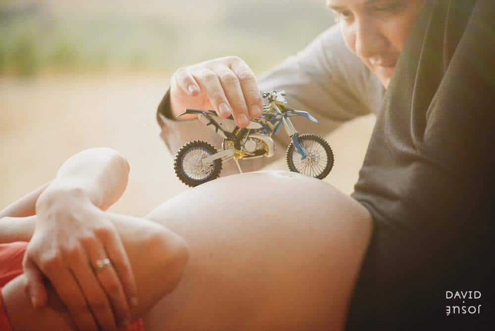 Expecting parents laughing with a toy motorcycle during a playful maternity session