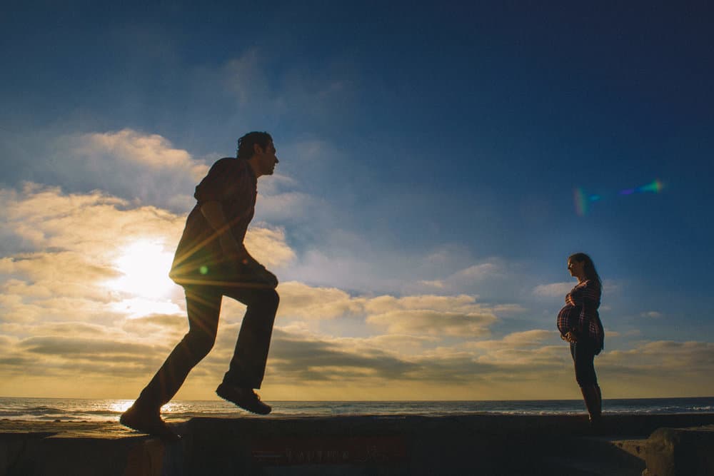 Expecting couple walking hand in hand along the shoreline at golden hour