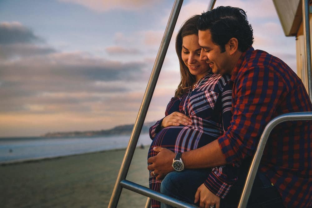 Expecting parents walking the beach at sunset — family and maternity photography by David Josué