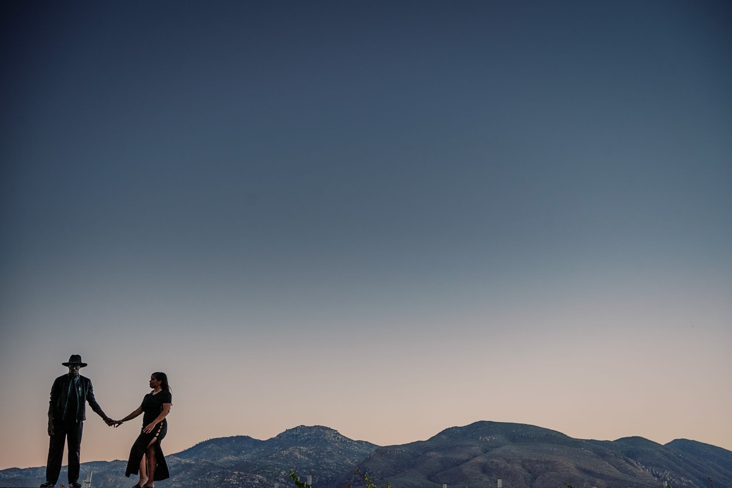Engaged couple holding hands at dusk against the hills — engagement photography by David Josué