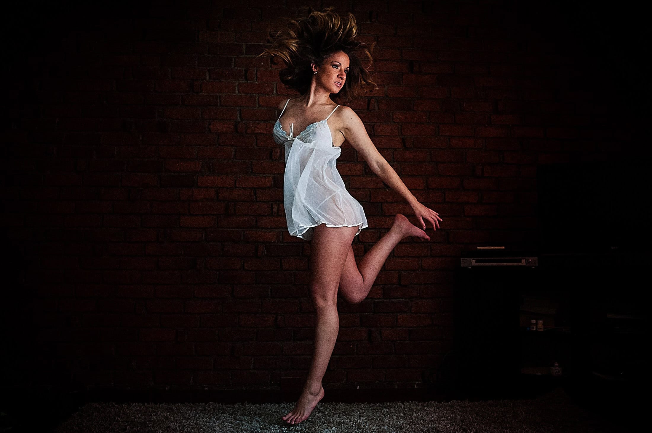 Woman in a white babydoll jumping on the bed, laughing mid-air — boudoir session by David Josué